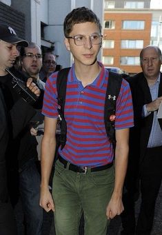 a young man wearing glasses and a striped shirt is walking in front of a group of people