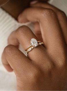 a woman's hand with a diamond ring on her left hand and the other hand holding an engagement ring