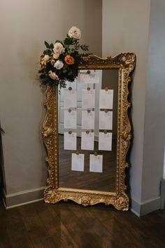 a gold framed mirror sitting on top of a wooden floor next to a vase with flowers