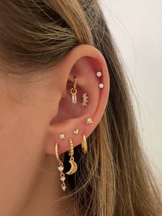 a woman wearing ear piercings with stars and moon charms on her ears, both in gold or silver