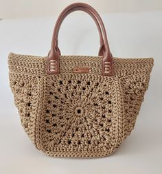 a crocheted handbag sitting on top of a white table next to a brown leather handle