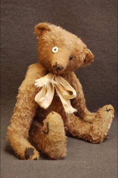 a brown teddy bear sitting on top of a gray floor next to a black wall