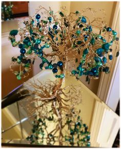 a tree with blue and green beads on it's branches in front of a mirror