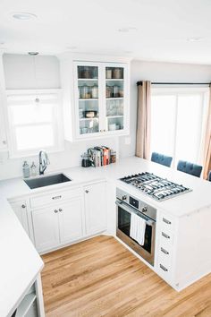 a kitchen with white cabinets and wood flooring is pictured in this image, there are two windows above the stove