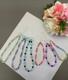 four different colored beads are hanging on a white surface next to flowers and a bouquet