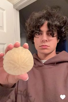 a young man holding up a piece of wood in front of his face and wearing a brown hoodie