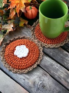 two crocheted coasters sitting on top of a wooden table next to a green mug