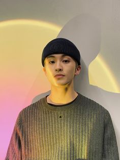 a young man standing in front of a wall wearing a beanie and looking at the camera