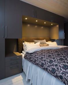 a large bed in a bedroom next to some cupboards and drawers on the wall