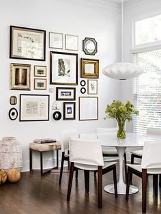 a dining room table with white chairs and pictures on the wall in front of it