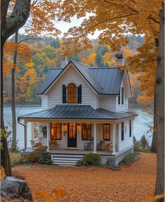 a white house surrounded by trees with leaves on the ground and water in the background