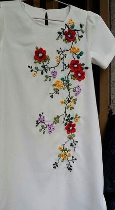 a white t - shirt with colorful flowers on it hanging from a clothes line in front of a door