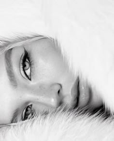 a black and white photo of a woman's face with fur on the bed