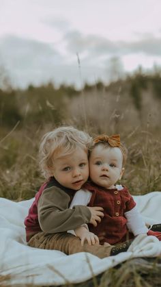 two toddlers sitting on top of a blanket in the middle of a grassy field