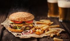 a hamburger and french fries on wax paper with beer in the backgroung