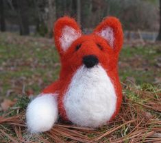 a red and white stuffed animal laying on top of dry grass next to trees in the woods