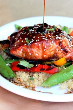 a white plate topped with meat and veggies covered in sesame seed sauce being drizzled over it