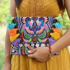 a woman wearing a yellow dress holding a colorful embroidered clutch with flowers and birds on it