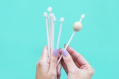 a person holding several toothpicks in their hands on a blue background with pink nail polish