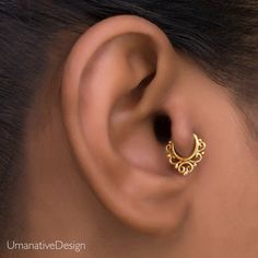 a woman's ear is shown with an intricate gold nose ring in the shape of a crescent