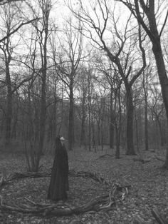 a woman standing in the middle of a forest surrounded by dead branches and bare trees