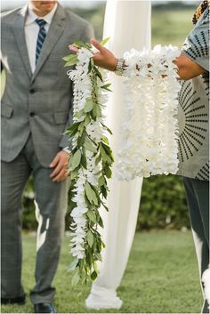 a man and woman standing next to each other in front of a white arch with flowers on it