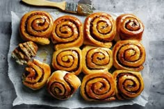 some cinnamon rolls are on a piece of parchment paper with a paintbrush next to them