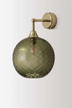 a green glass wall light hanging from the side of a white wall with a gold finish