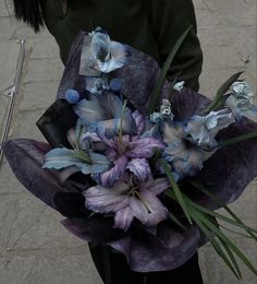 a woman holding a bouquet of flowers in her hands on the sidewalk with an umbrella nearby