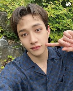 a young man is making the middle finger sign with his hand while sitting in front of some bushes