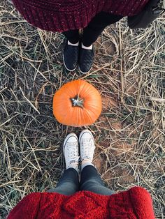 two people standing next to each other in the grass with pumpkins on their feet