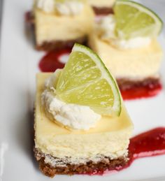 three pieces of cheesecake on a plate with limes and red sauce around them