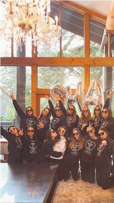 a group of women posing for a photo in front of a chandelier and window