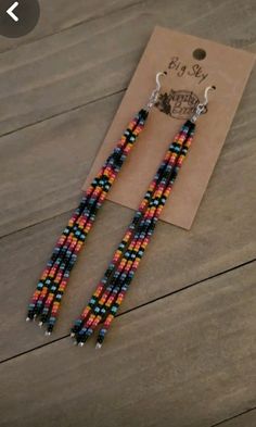 a pair of beaded earrings sitting on top of a wooden table next to a tag