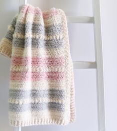 a knitted blanket sitting on top of a white chair next to a wooden ladder