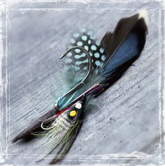 two flies with feathers attached to them sitting on a wooden table next to each other