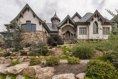 a large house sitting on top of a lush green hillside next to rocks and trees