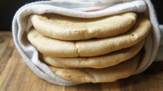 a stack of uncooked bread on top of a wooden table next to a cloth bag