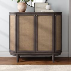 a brown cabinet sitting next to a mirror on top of a wooden floor with a plant in it