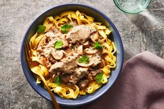 a blue bowl filled with pasta and meat covered in sauce next to a glass of water