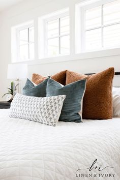 a bed with two pillows on top of it and three windows above the headboard