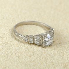 an antique style diamond ring sits on the sand, with three stones in it's center