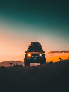 a jeep driving through the desert at sunset with its headlights on and fog in the air