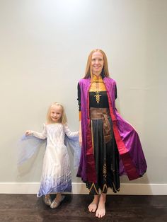 two children dressed up as princesses standing next to each other in front of a wall