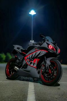 a red and black motorcycle parked in a parking lot next to a street light at night