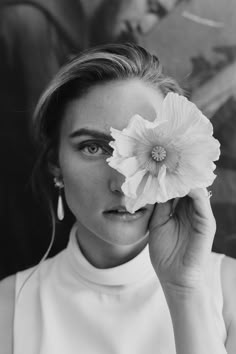 a black and white photo of a woman holding a flower in front of her face