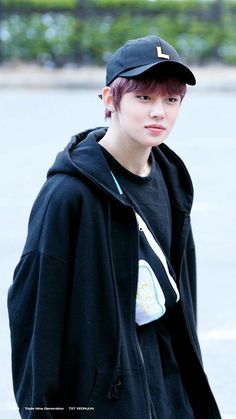 a young man wearing a black baseball cap and hoodie standing in front of a parking lot