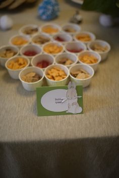 a table topped with cups filled with different types of food next to a small card