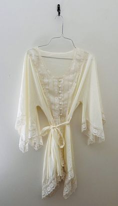 Indulge in vintage charm with this stunning 70s Val Mode lingerie short robe / nightgown . The satiny cream fabric is beautifully accented with delicate lace trim, a tie waist, and button front adding a touch of sleek sophistication to your sleepwear routine. This original piece is perfect for anyone looking to add a unique touch to their wardrobe. Can be worn in the bedroom or out! Crafted with high-quality nylon material, this robe is both comfortable and durable. The ivory color and regular size type make it a versatile addition to any vintage clothing collection. Made in the United States, this original piece is a must-have for any fashion-forward individual. Sized as a medium but does run small. Fits more like a small. Measurements: Length 30" Shoulder to shoulder 15" Waist 14" Lace Robe With Lace Trim For Sleep, Lace Sleep Robe With Lace Trim, Lace Trim Sleep Robe, Cottagecore White Sleepwear With Lace Trim, White Cottagecore Sleepwear With Lace Trim, Feminine Cream Nightgown With Lace Trim, White Lace Trim Robe For Summer, Cream Lace-trim Sleepwear For Wedding, Cream Wedding Sleepwear With Lace Trim