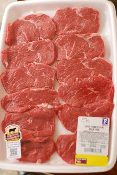 raw meat is displayed in a white tray on a table with price tags attached to it